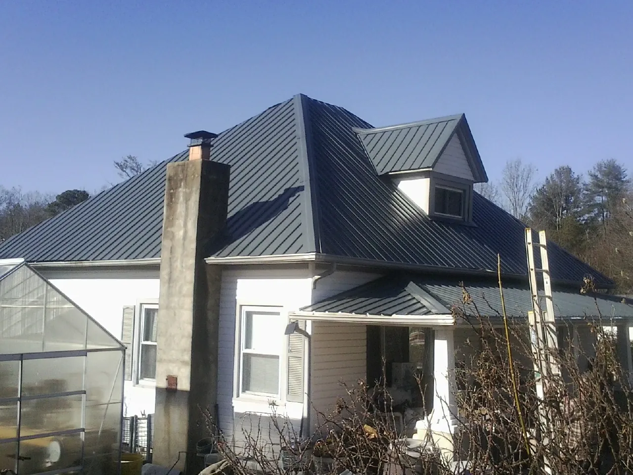Dark blue standing seam metal roof on a white farmhouse with dormer — Slate & Tile Roof Repair by Roofing Brothers in Bellport