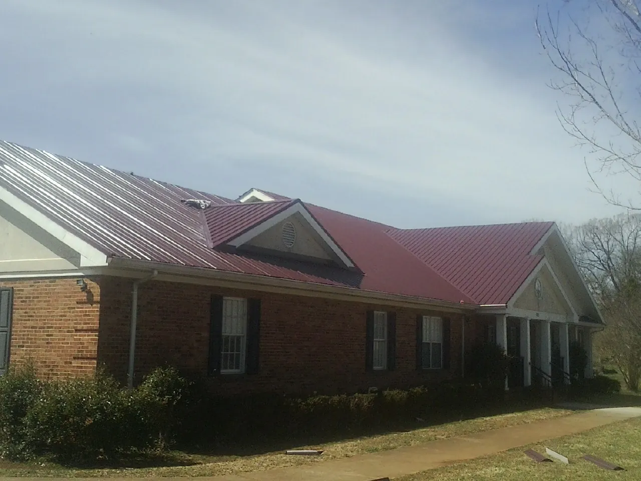 Red metal roof with gabled entries on a long brick building, from a Hail Damage Roof Repair job in Bellport