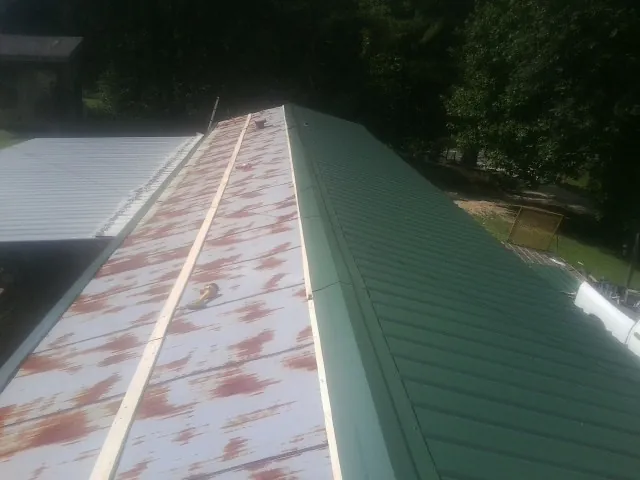 Old rusted panels beside newly installed green metal roofing — Wind Damage Roof Repair by Roofing Brothers in Bellport