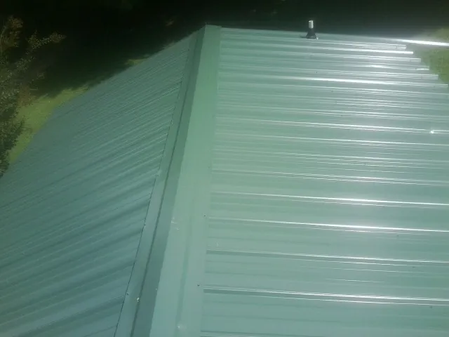 New green metal panels meeting at the ridge of a roof — Flat Roof Repair work by our crew in Bellport