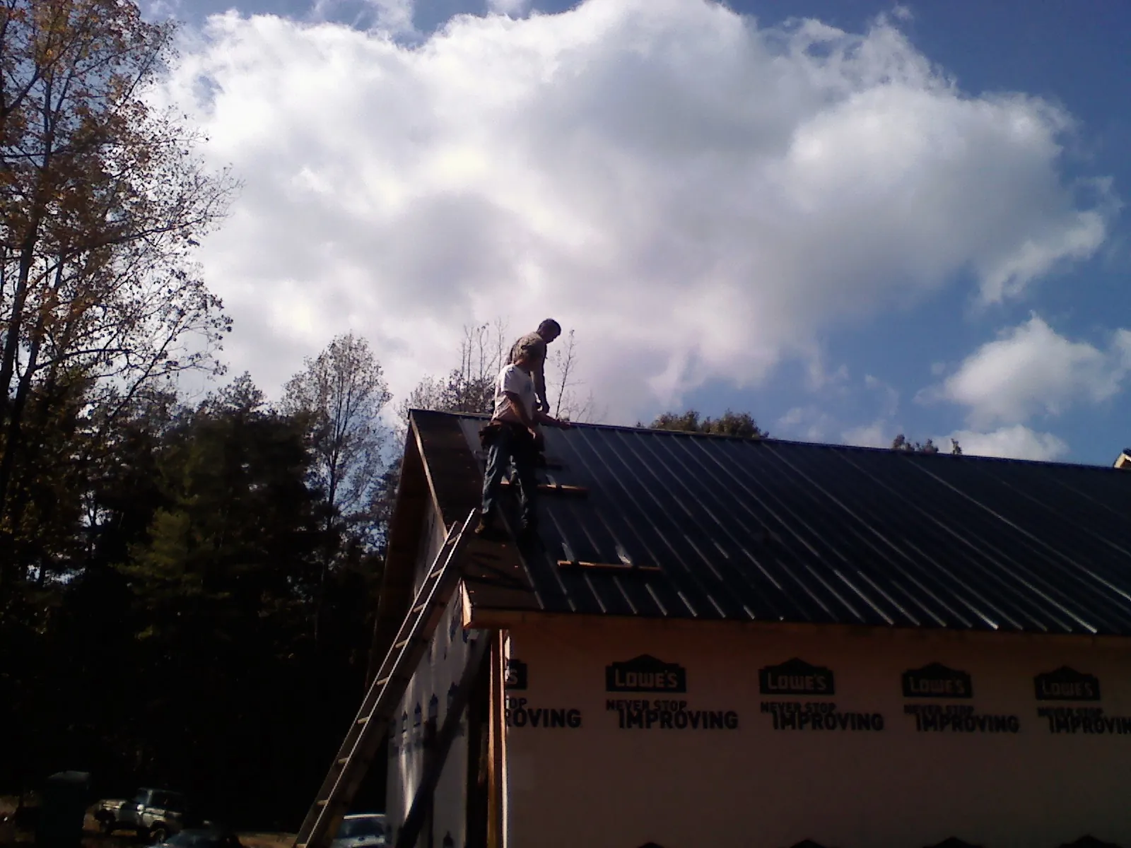 Roofer fastening dark metal panels high against a cloudy sky, from a Roof Inspection job in Bellport