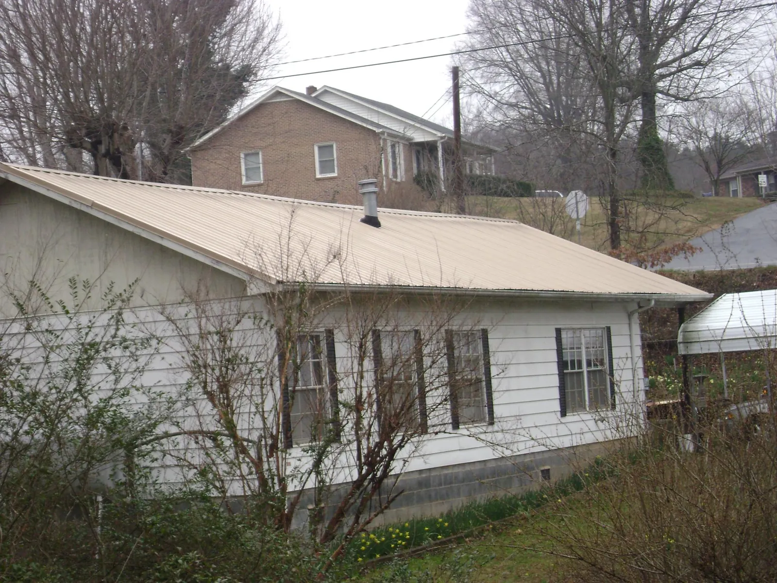 Tan metal roof on a white sided house set into a hillside — Commercial Roofing by Roofing Brothers in Bellport